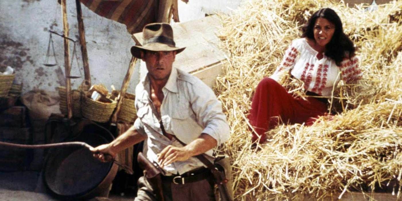 Indiana Jones empunha um chicote enquanto Marion está atrás dele em uma montanha de feno em Raiders of the Lost Ark