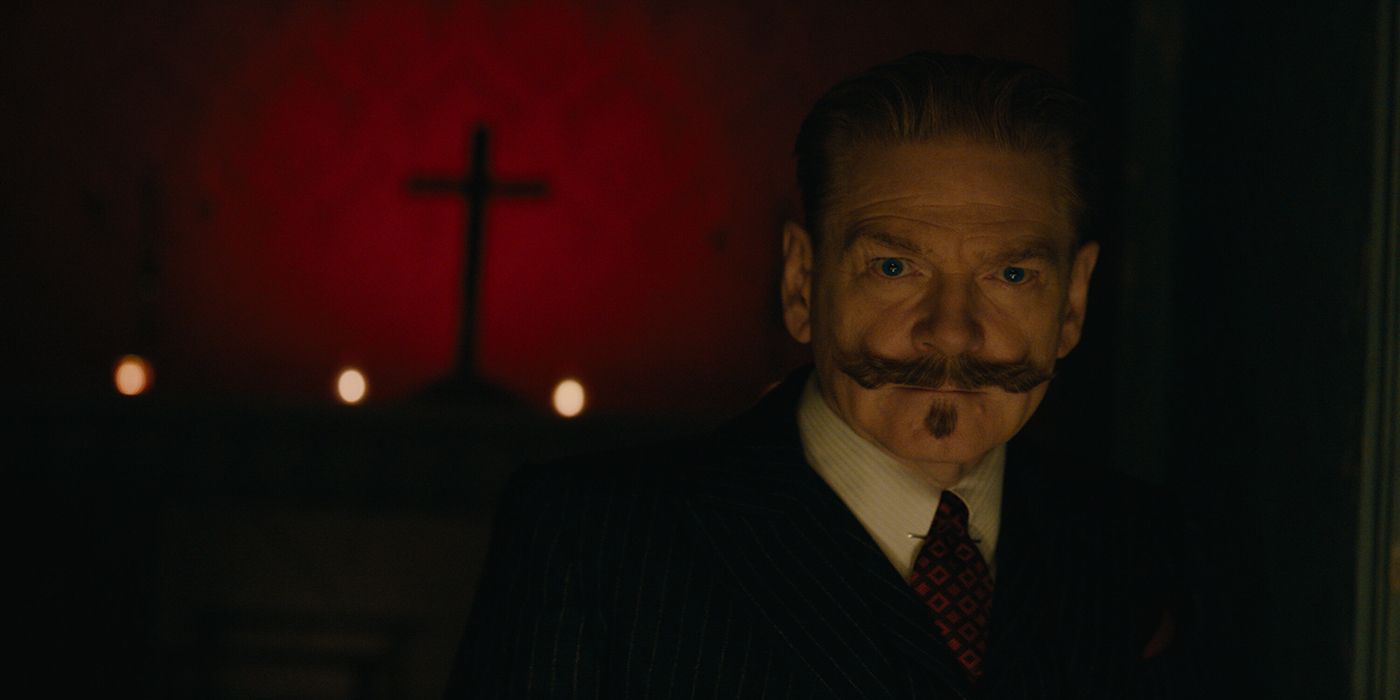 Kenneth Branagh as Hercule Poirot standing in a dark room with the shadow of a cross behind him