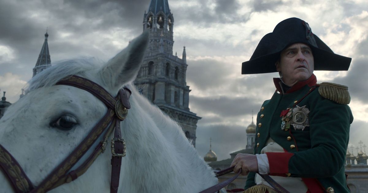 A close-up low-angle shot of Joaquin Phoenix as Napoleon riding a white horse.