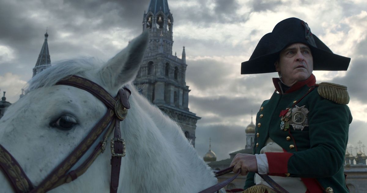 Um close-up em ângulo baixo de Joaquin Phoenix como Napoleão cavalgando um cavalo branco.