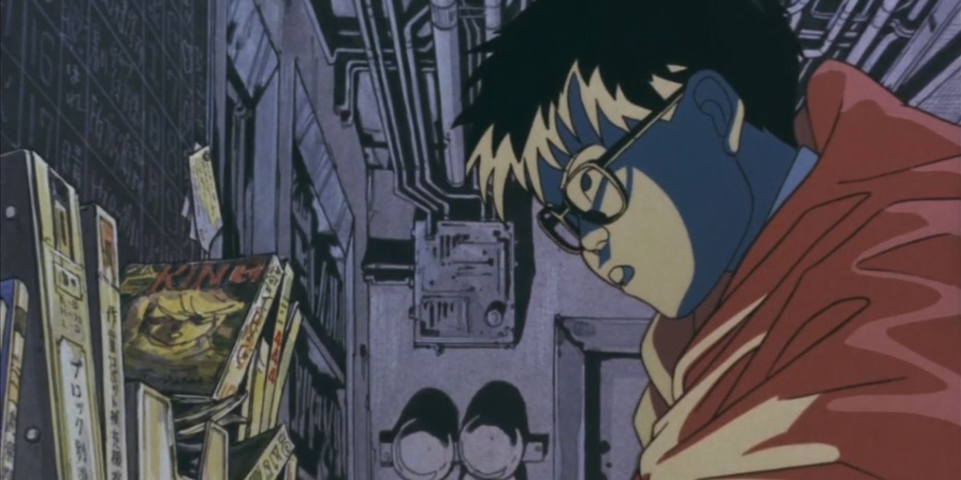 A young man with glasses browses a shelf of books in some sort of factory room.