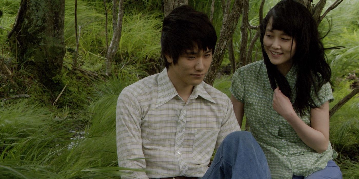 Um jovem casal japonês está sentado na grama alta de uma pequena floresta.