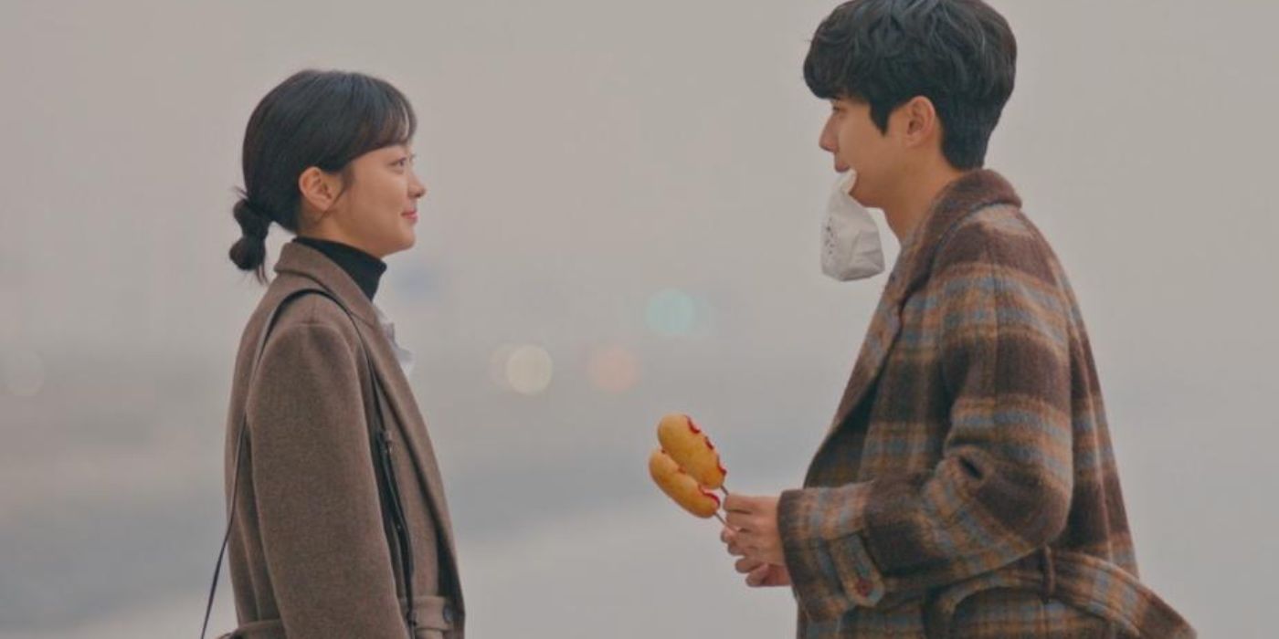 A Korean man holds two corndogs, and a Korean woman grins at him