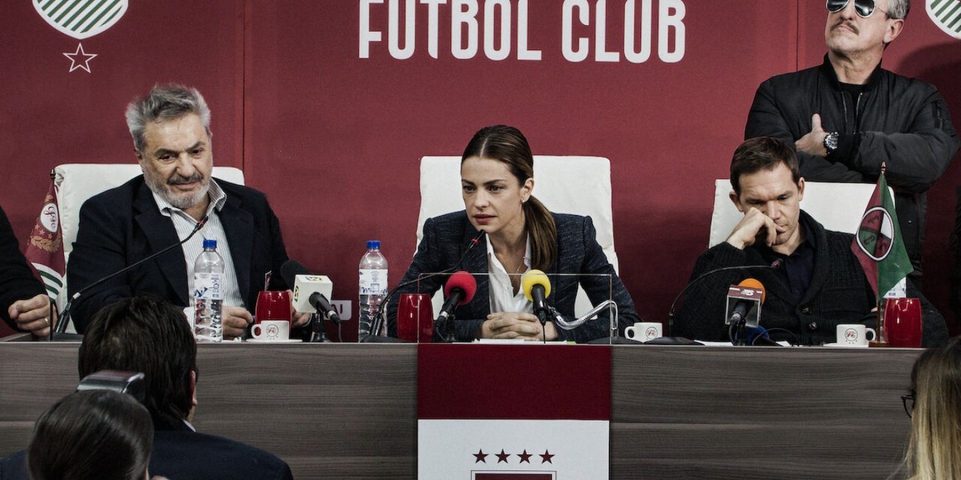 Uma mulher de aparência severa está no centro da coletiva de imprensa de um clube de futebol.