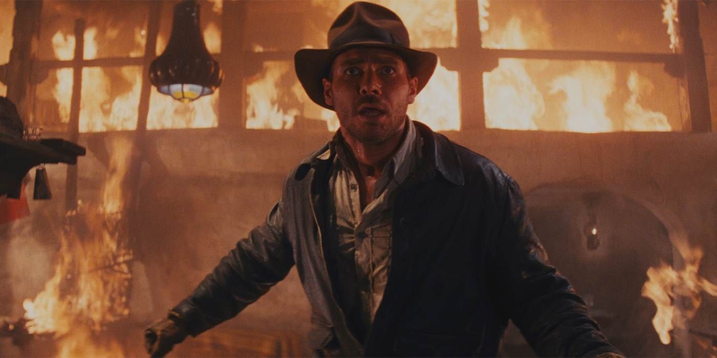 Indiana Jones looks shocked when being shot at while a building burns behind him in raiders of the lost ark