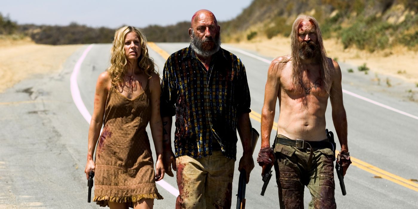 Two haggard-looking men and a bloodied woman walk along the side of a desert highway, armed with various guns