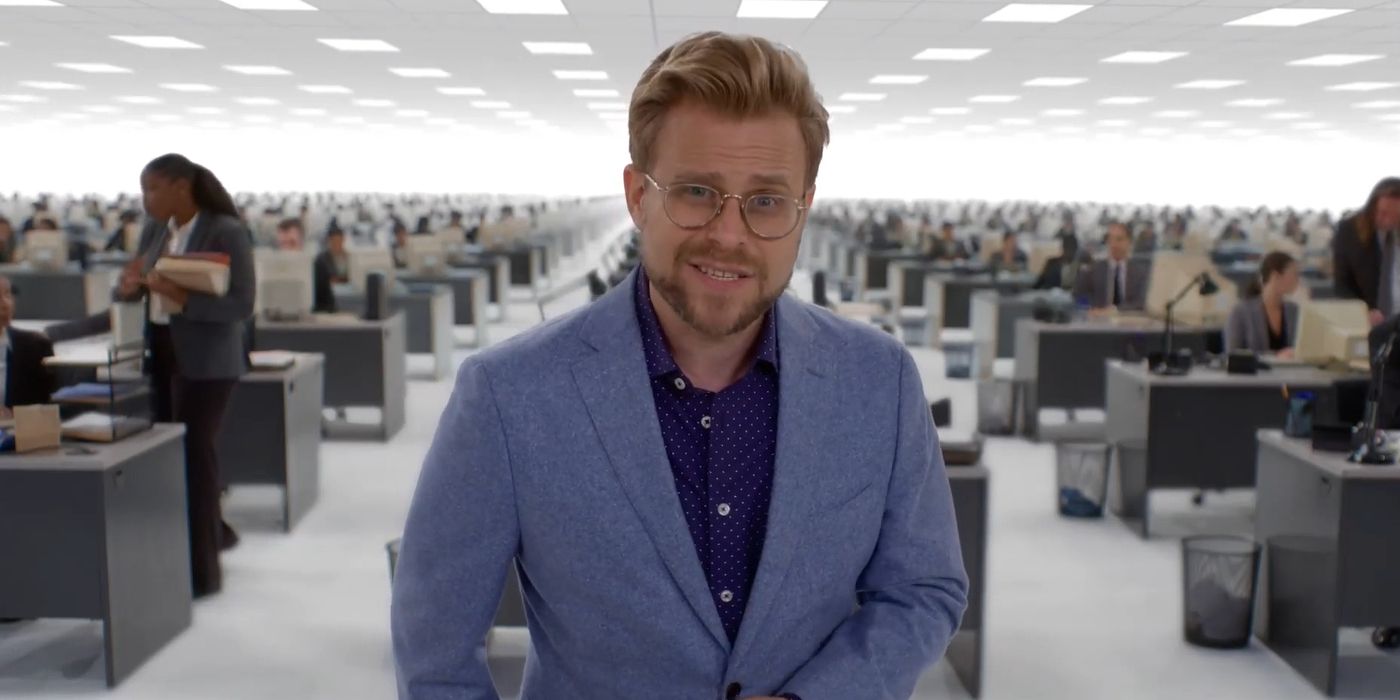 Adam stands in an office in The G Word With Adam Conover