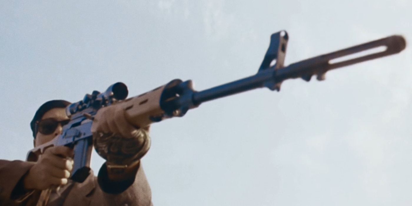 A low-angle shot of a man in dark sunglasses aiming a rifle at something off-screen
