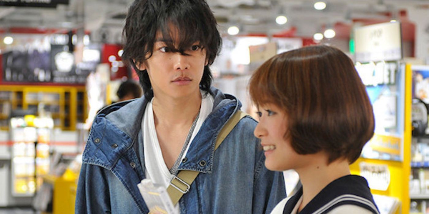 Um jovem japonês encara uma jovem japonesa, que sorri para algo fora do quadro