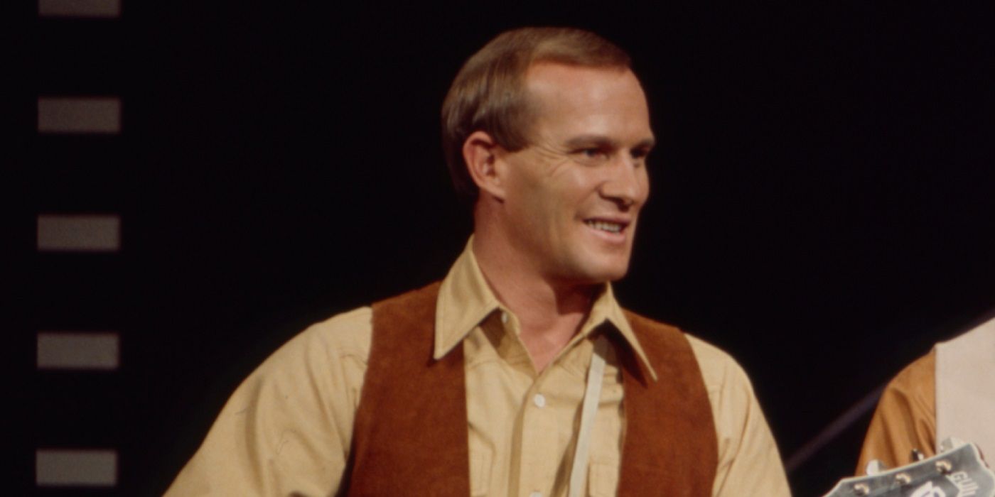 Tom Smothers wearing a waistcoat, holding a guitar