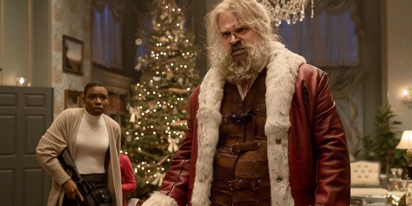 David Harbour as Santa Claus is fed up in Violent Night standing in a room with a woman and a christmas tree