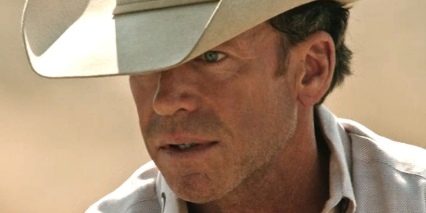 Taylor Sheridan wearing a tan shirt and cowboy hat, looking at someone off-screen in Yellowstone.