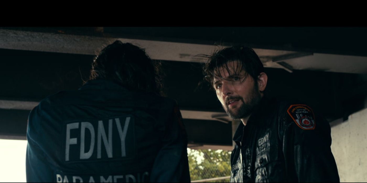 Adam Scott wearing a fire department jacket looking at something off-screen in the trailer for Madame Web