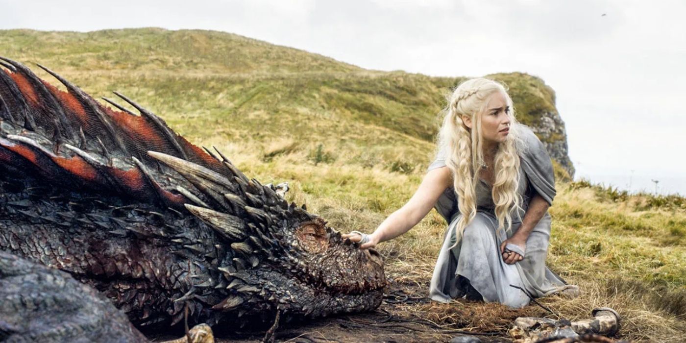 Emilia Clarke as Daenerys Targaryen with Drogon sitting in a field in Game of Thrones