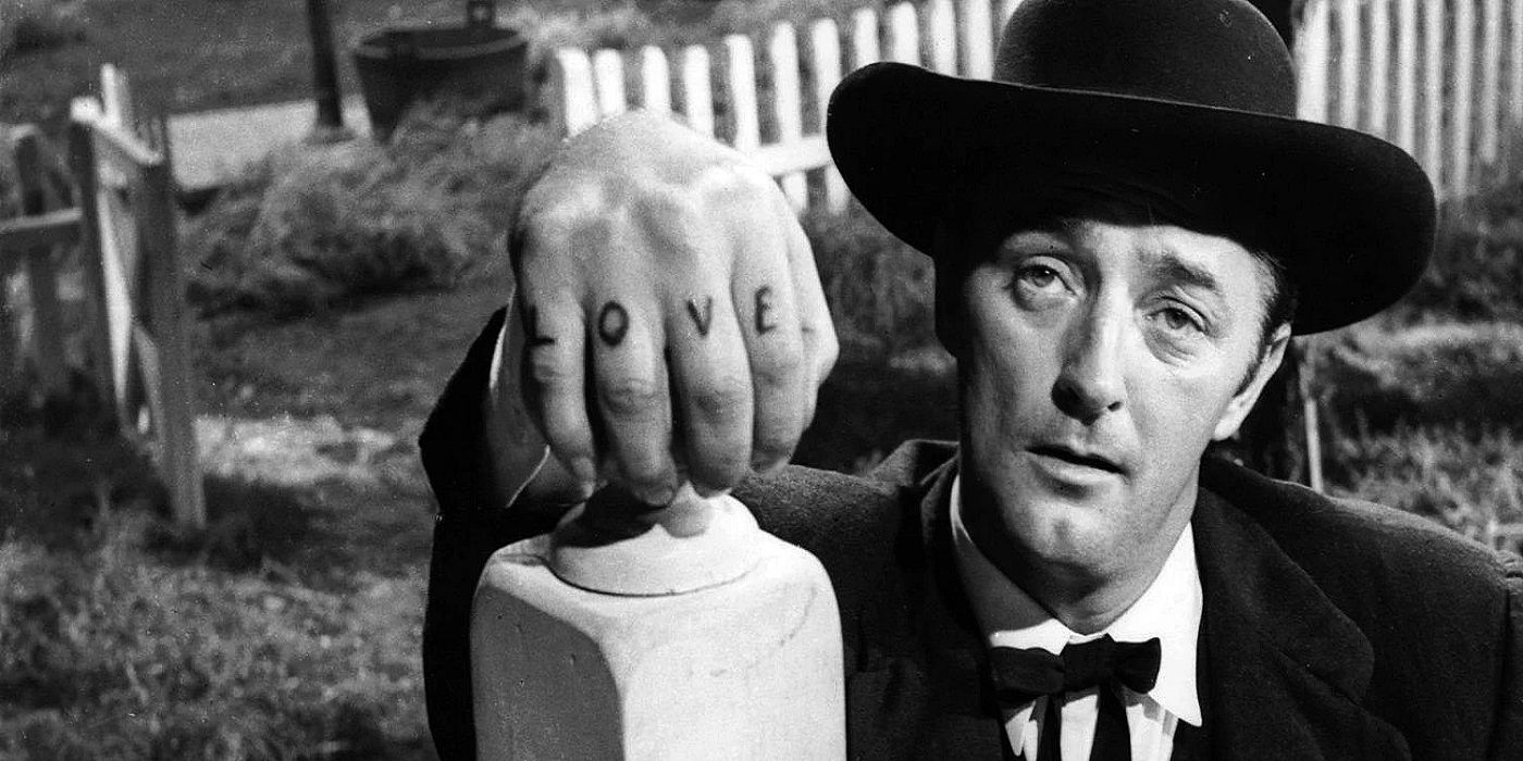 Robert Mitchum as Harry Powell wearing a dark suit with the word "love" written on his hand in The Night of the Hunter