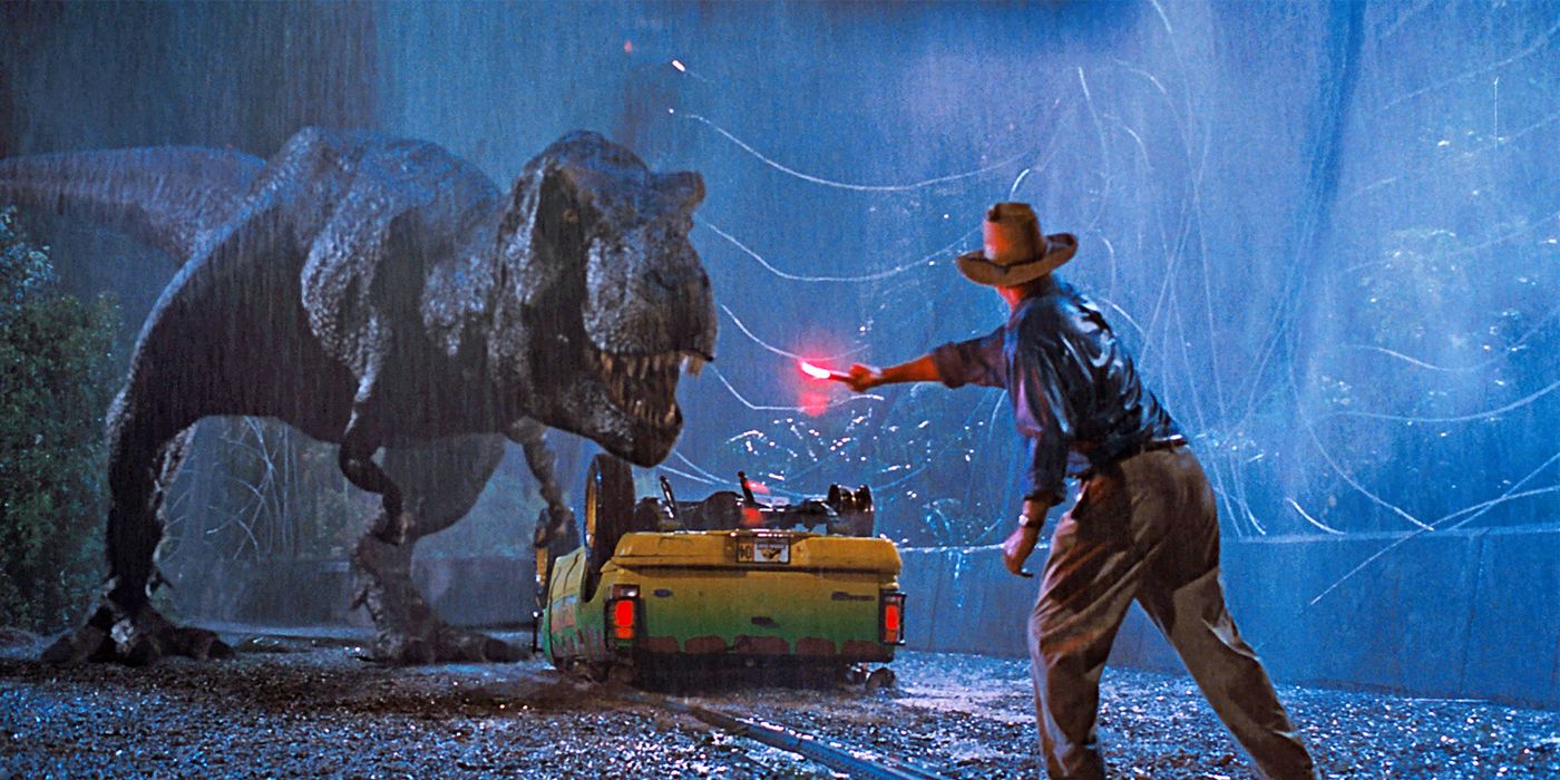 A T. rex is looking at Sam Neill as Alan Grant who is holding a torch in Jurassic Park
