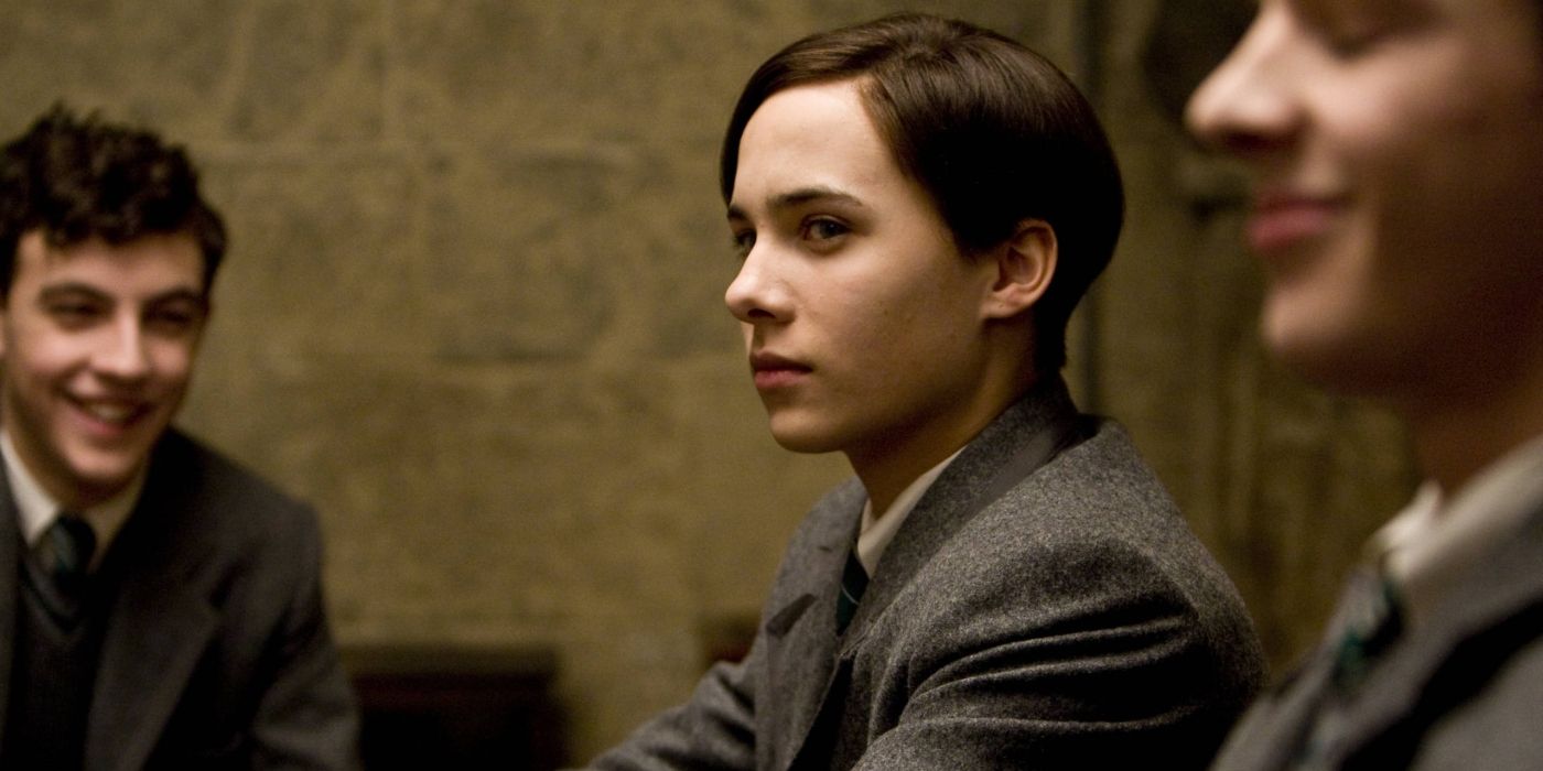 Frank Dillane as Tom Riddle, sitting reservedly while other boys around him laugh, in Harry Potter and the Half-Blood Prince