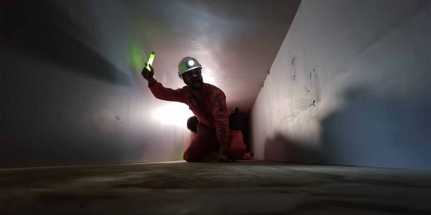 A maintenance worker crawls through a dark tunnel