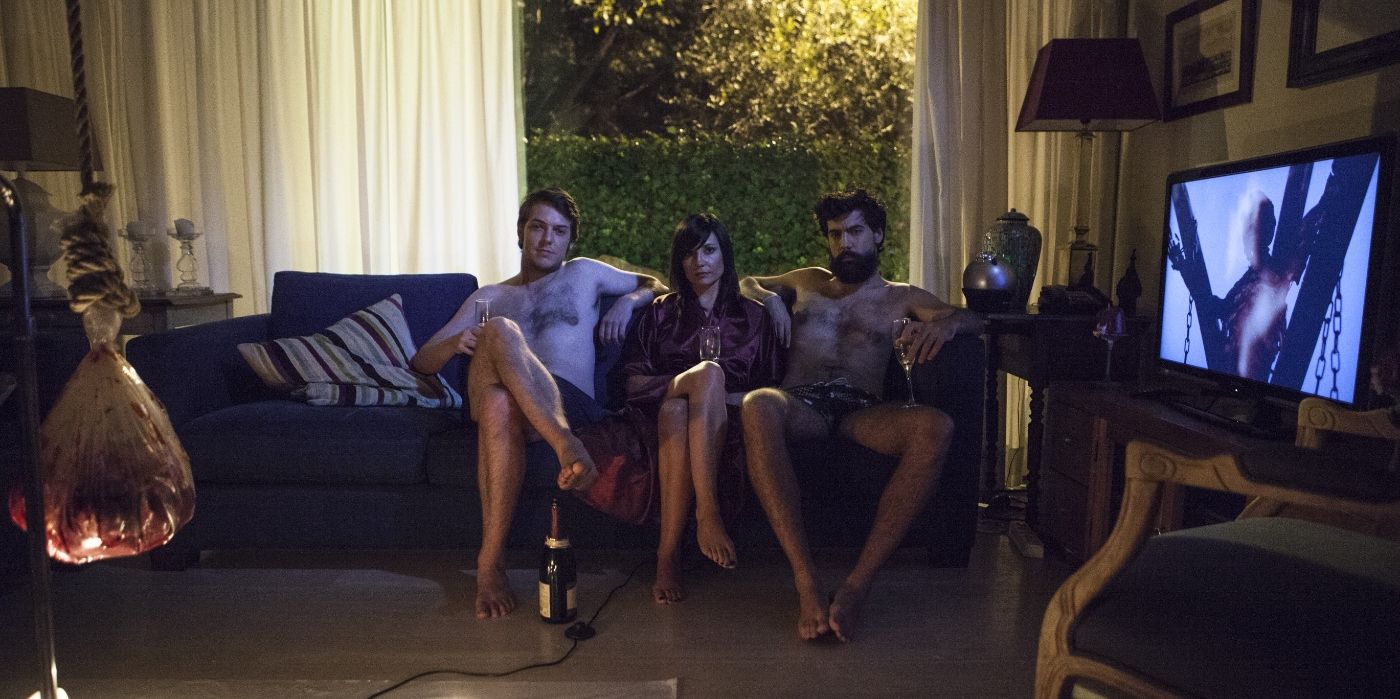 Two half-naked men and one woman cozying up on a sofa