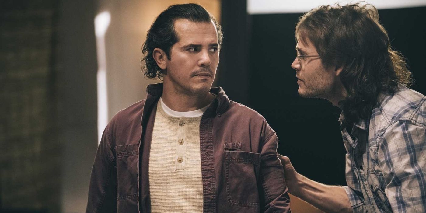 Taylor Kitsch as David Koresh wearing large glasses with long hair talking to John Leguizamo as Jacob Vazquez in Waco