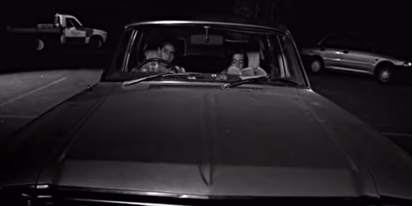 A black and white shot of two people sitting in a car in Two Cars, One Night (2004) 
