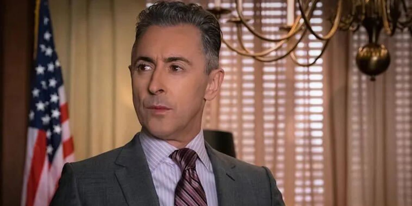 Alan Cumming as Eli Gold wearing a suit and tie with an American flag behind him in The Good Wife