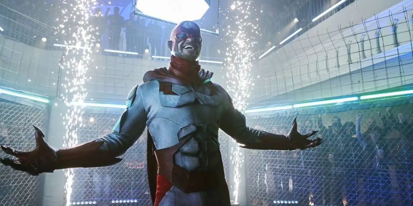 Alan Ritchson as Hawk smining and laughing in a cage with people cheering around him in Titans
