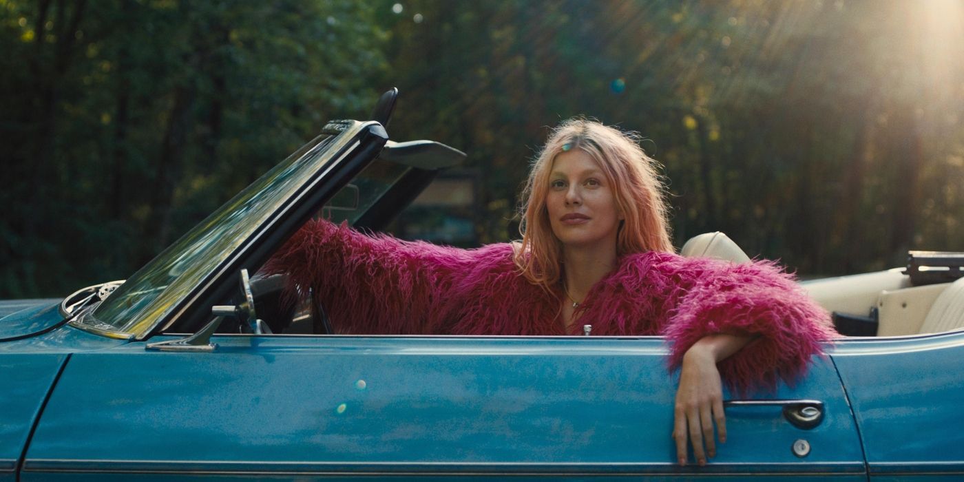 Camila Morrone as Marmalade wearing a pink fur jacket drives a blue car in Marmalade