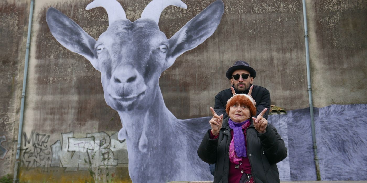 Agnès Varda and JR pose in front of a large goat mural