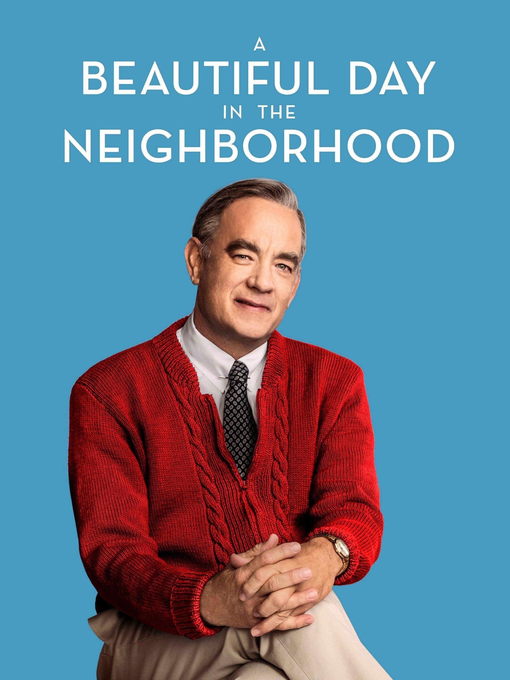 Tom Hanks as Fred Rogers wearing a red sweater smiling toward the camera in Beautiful Day in the Neighborhood