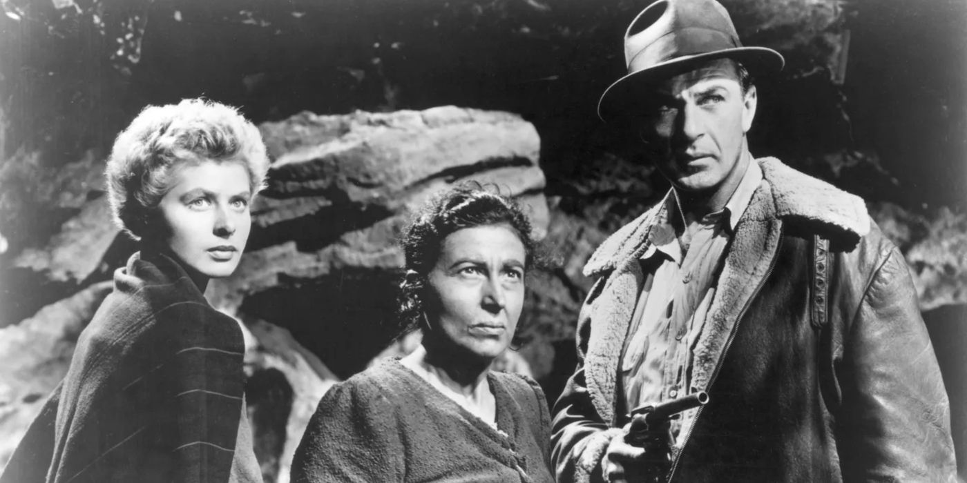 Ingrid Bergman, Katina Paxinou, and Gary Cooper holding a gun and standing in front of boulders  in For Whom the Bell Tolls