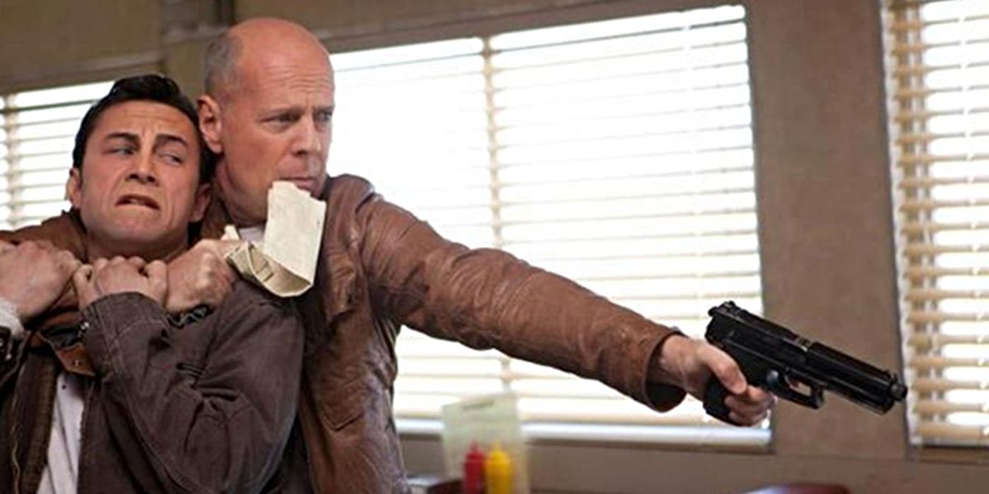 Joseph Gordon-Levitt as Joe, wearing a dark brown lighet, with Bruce Willis as Old Joe wearing a light brown jacket as the two are in a diner, and Old Joe points a pistol at someone off screen while Joe is in a chokehold in Looper