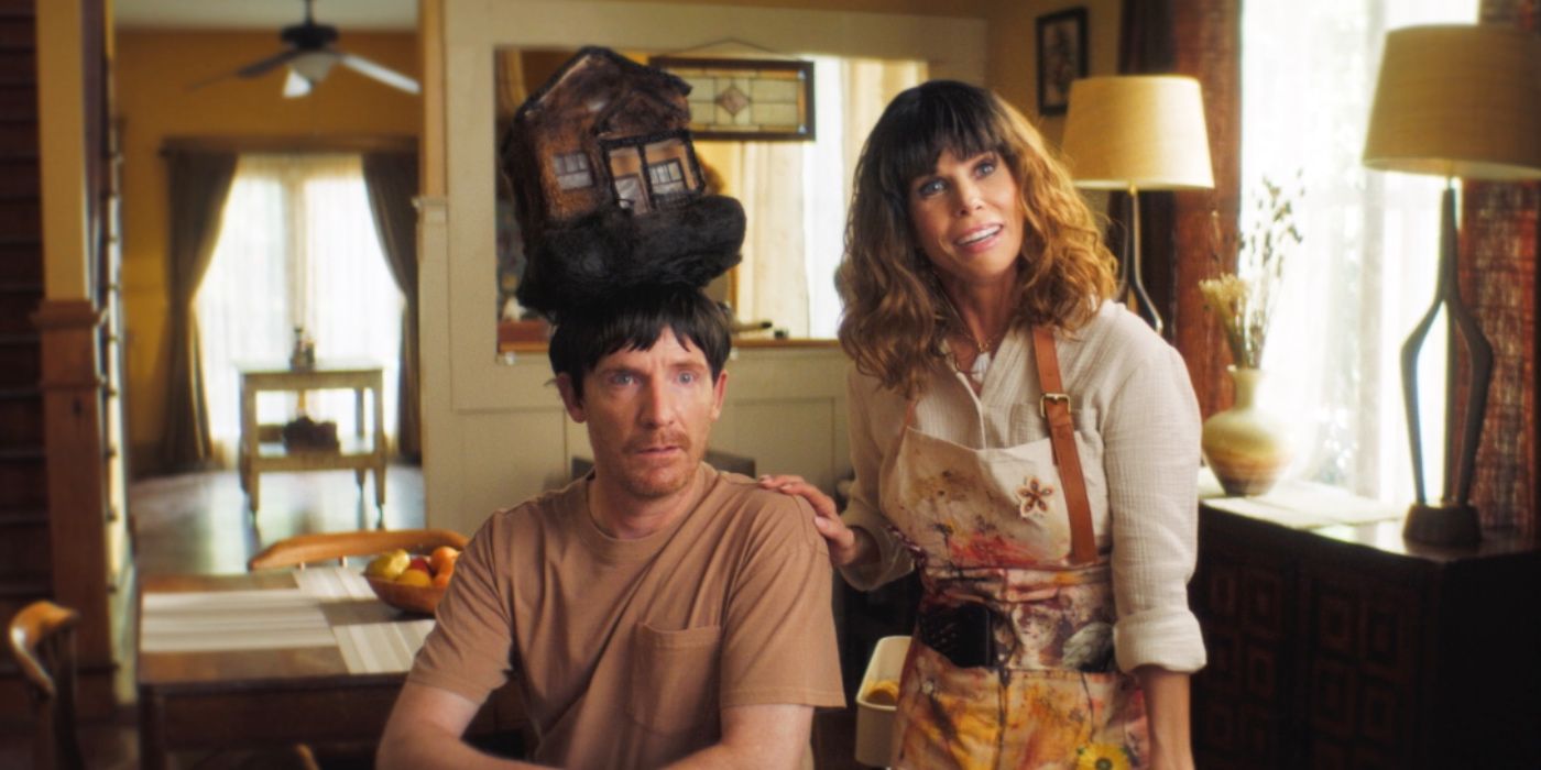 Cheryl Hines as Tammy with Mark Evan Jackason as Arhur wearing a wig standing at the dinner table in Popular Theory