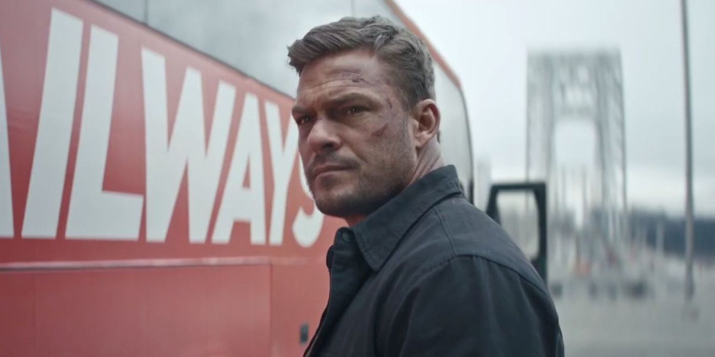 Alan Ritchson as Jack Reacher with cuts on his face standing next to a bus looking off-screen in Reacher