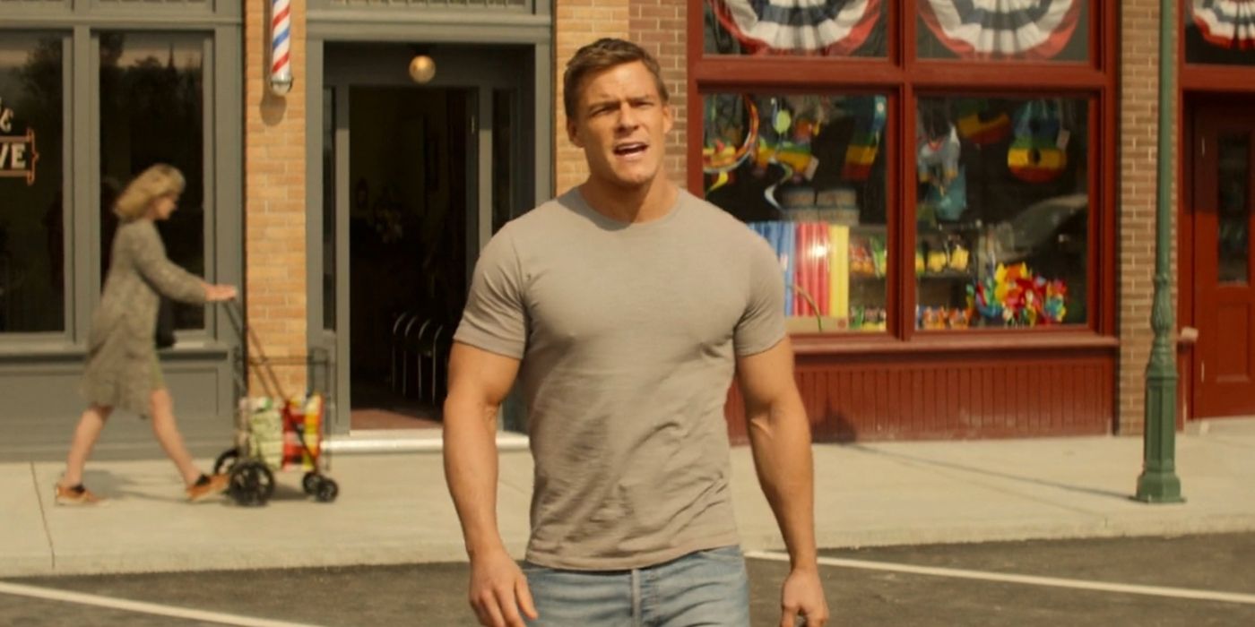 Alan Ritchson as Jack Reacher wearing a grey shirt and jeans walking out of a store talking to someone off-screen in Reacher