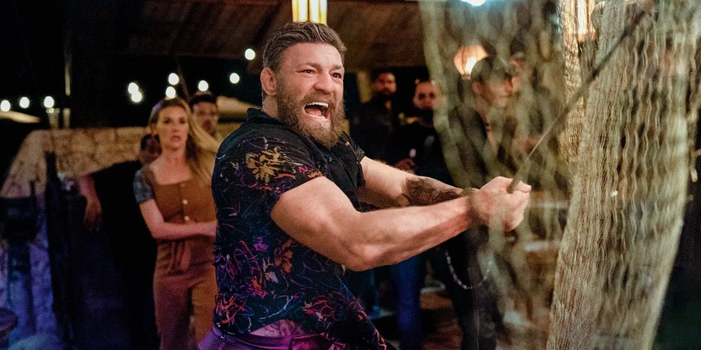 Conor McGregor in Road House yelling and smashing a fence with a pole.