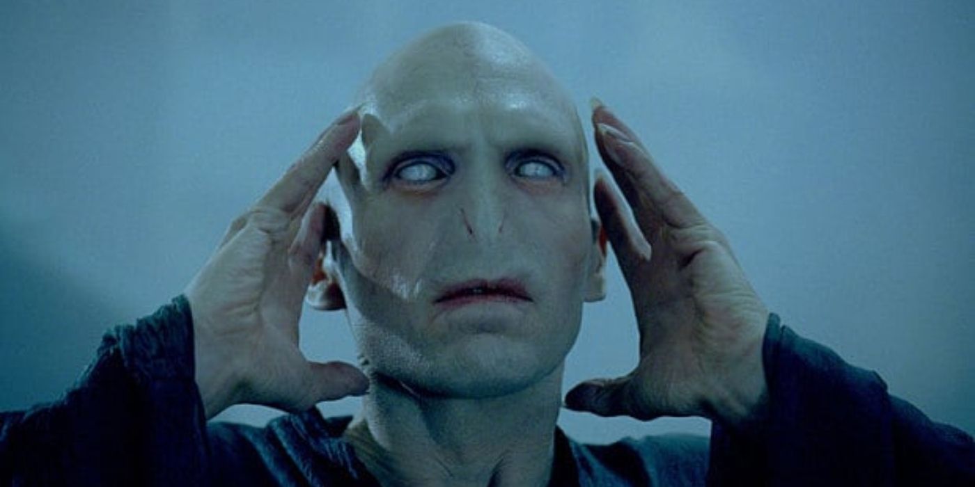 Ralph Fiennes as Voldemort with no nose and no hair holding his head with white eyes in Harry Potter