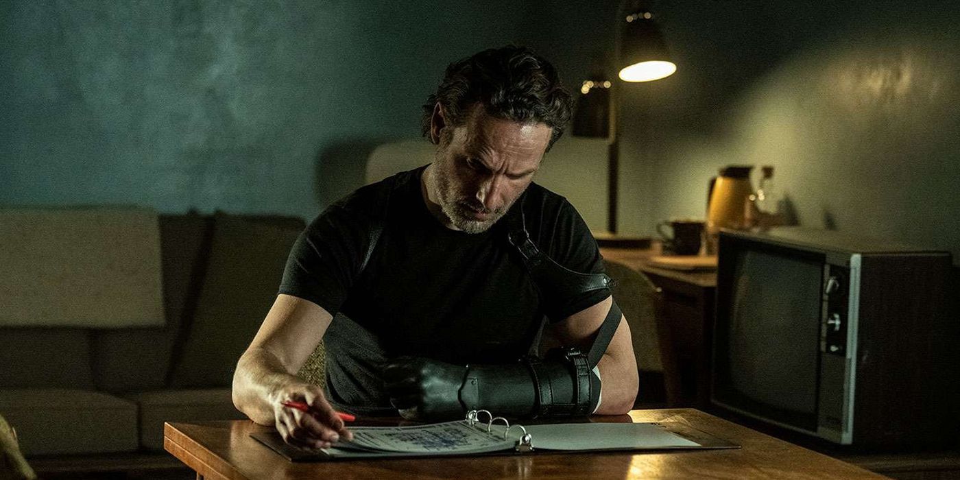 Rick sitting at a desk reading a binder with a prosthetic on his hand in The Walking Dead: The Ones Who Live.