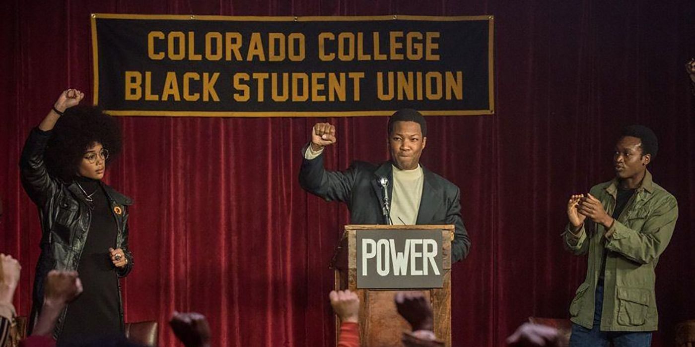 Corey Hawkins standing behind a podium, fist in the air in a scene from Black KkKlansman.