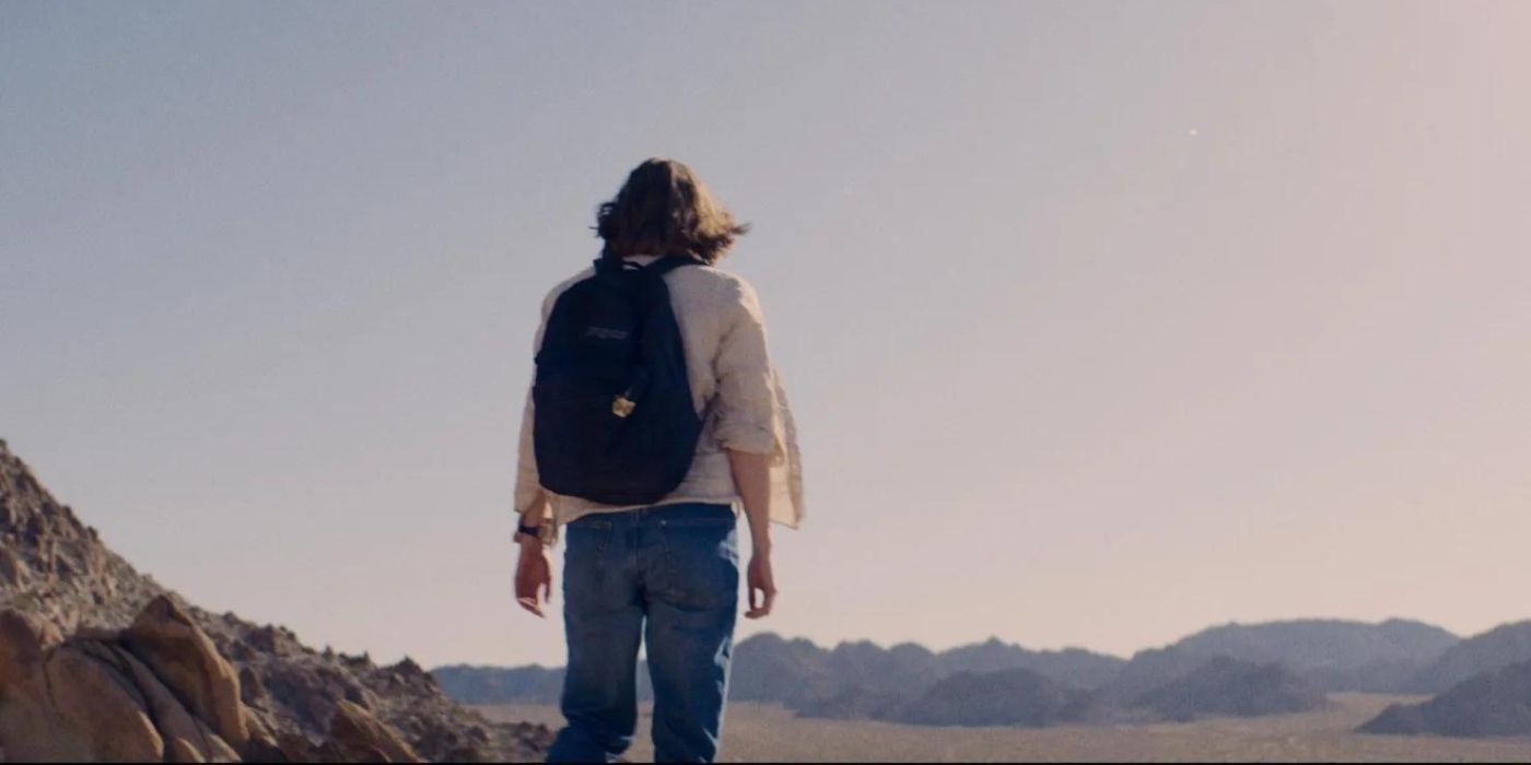 A shot from behind a woman with a backpack staring out into the open desert