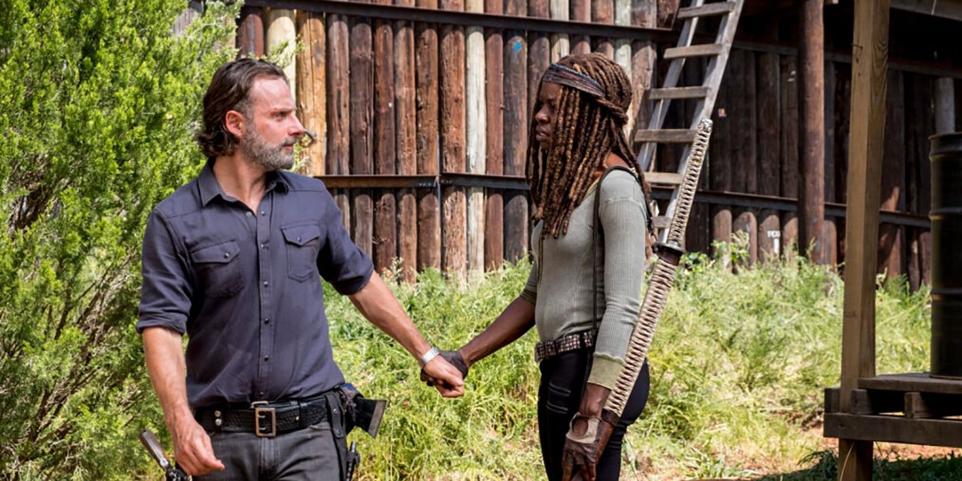 Rick and Michonne holding hands near a large fence and outpost on The Walking Dead