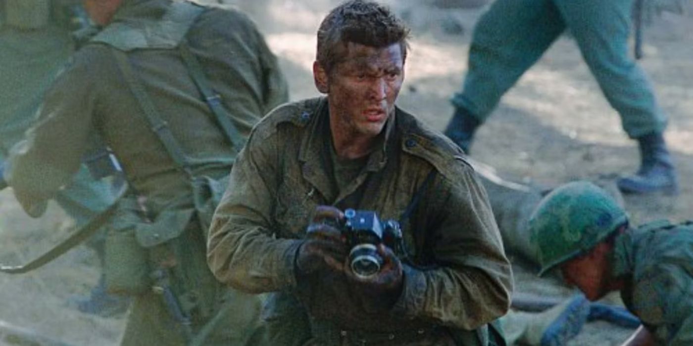 Barry Pepper as Joe Galloway with a camera in his hands taking photos with other soldiers in green uniforms behind him in We Were Soldiers