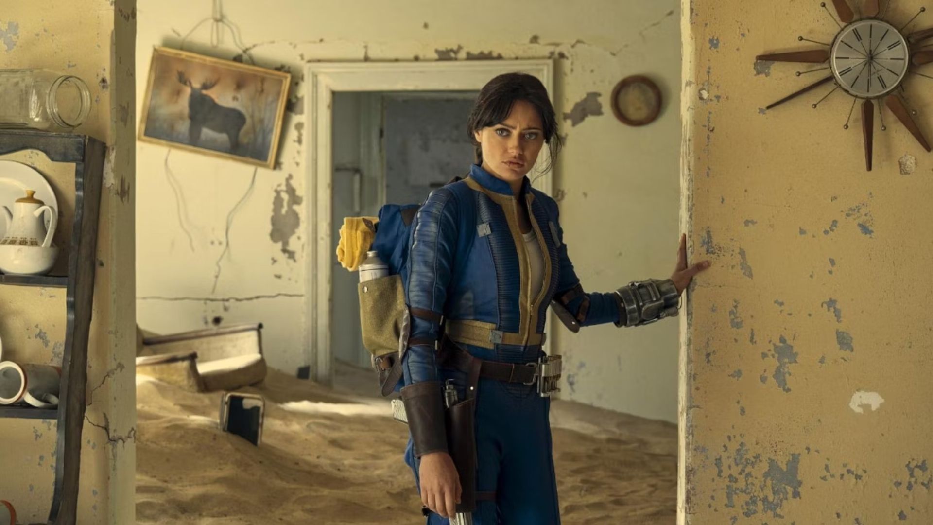 Ella Purnell as Lucy in Fallout wearing her vault tec suit walking through an abandoned house