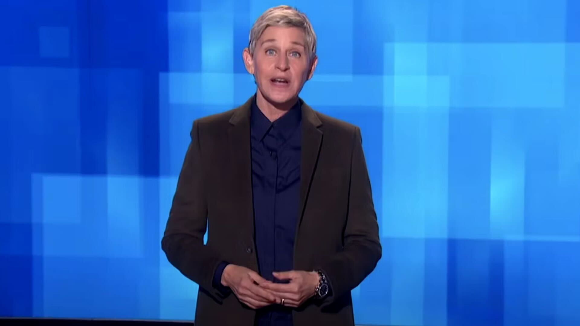 Ellen DeGeneres with hands together on a blue background
