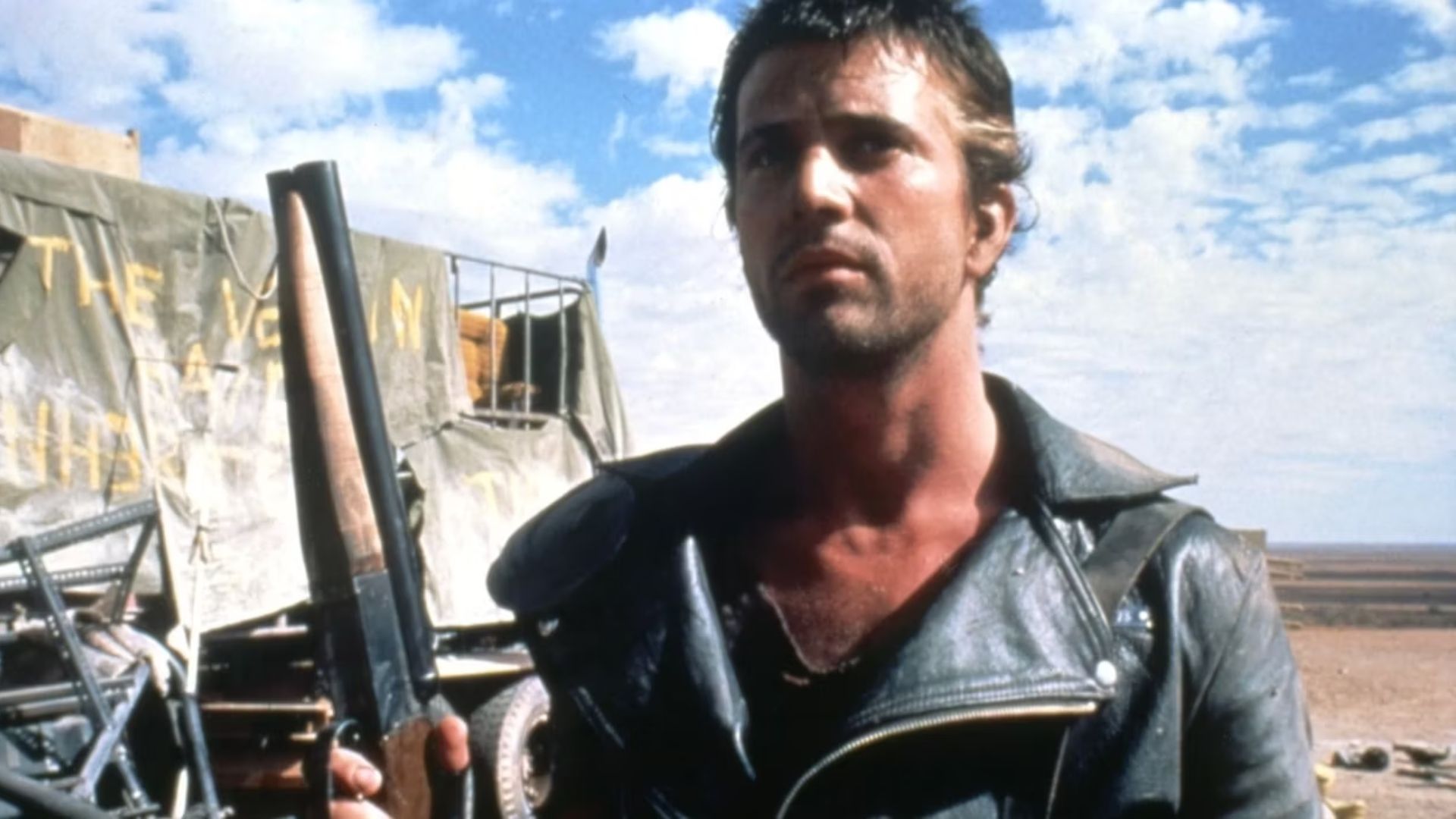 Mel Gibson in Mad Max 2: The Road Warrior holding a sawed-off shotgun wearing a leather jacket 