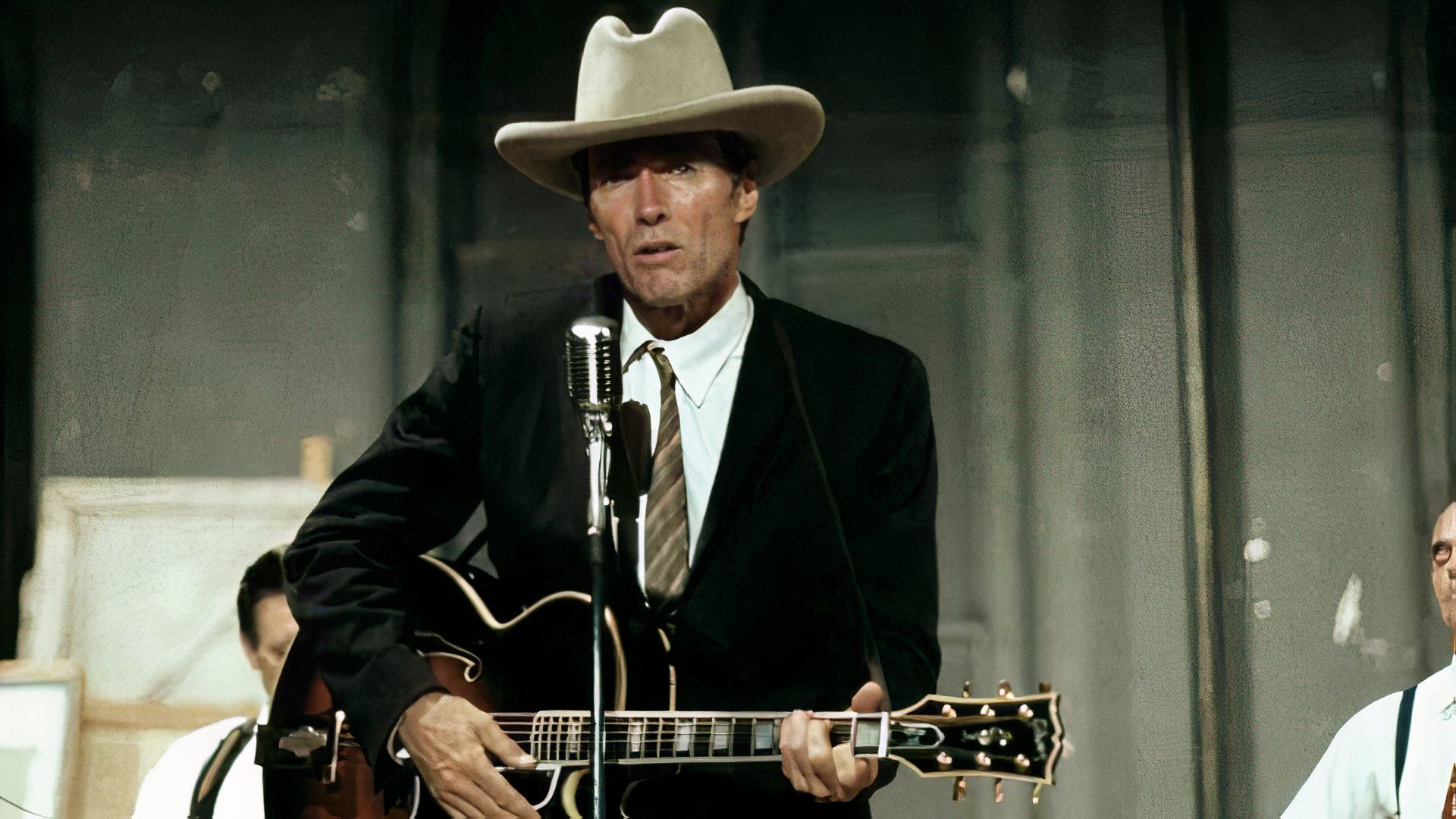 Clint Eastwood on stage with a guitar and white hat performing a song