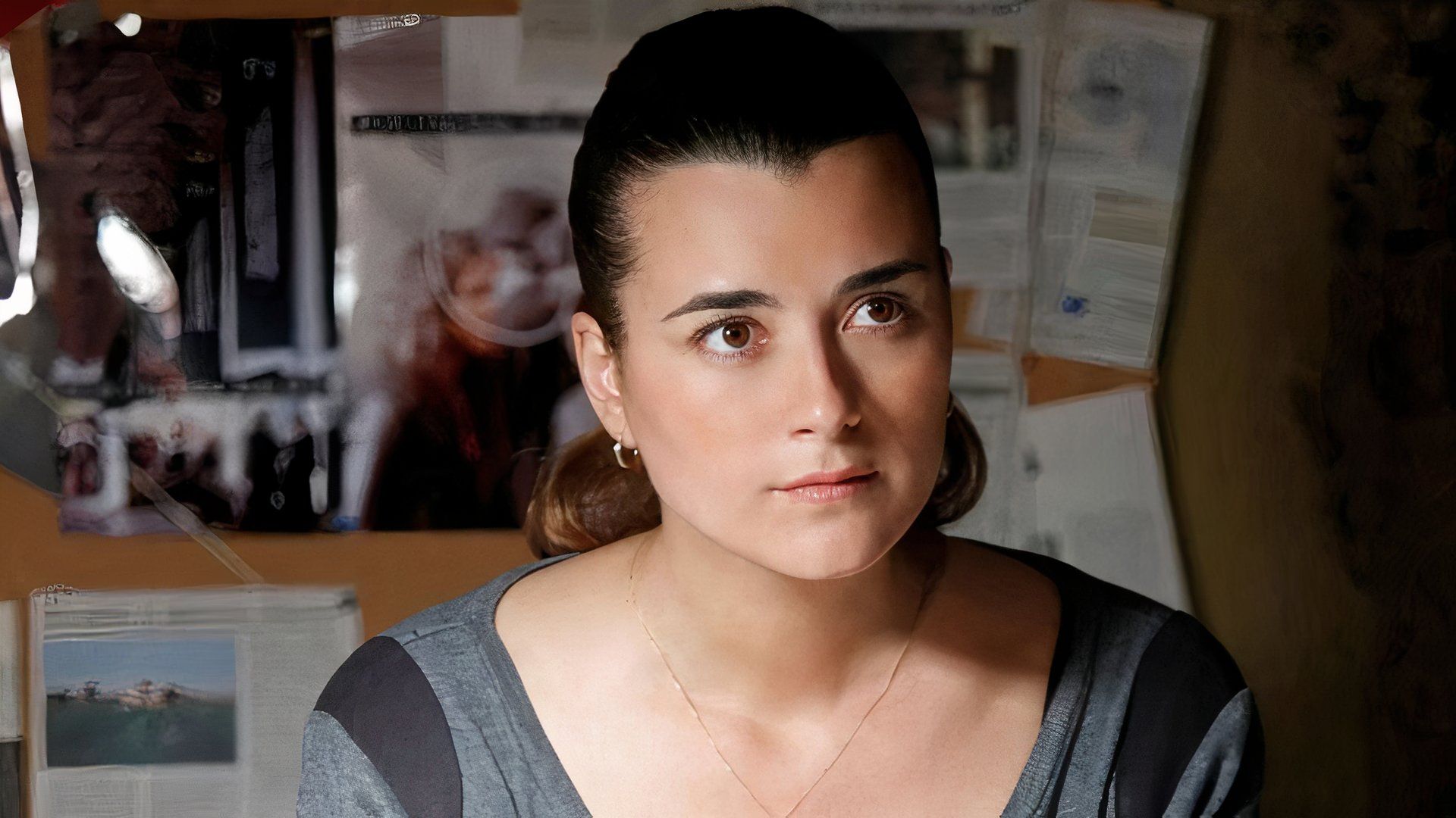 Cote de Pablo as Ziva David sitting at a desk with papers hung up behind her in NCIS (1)