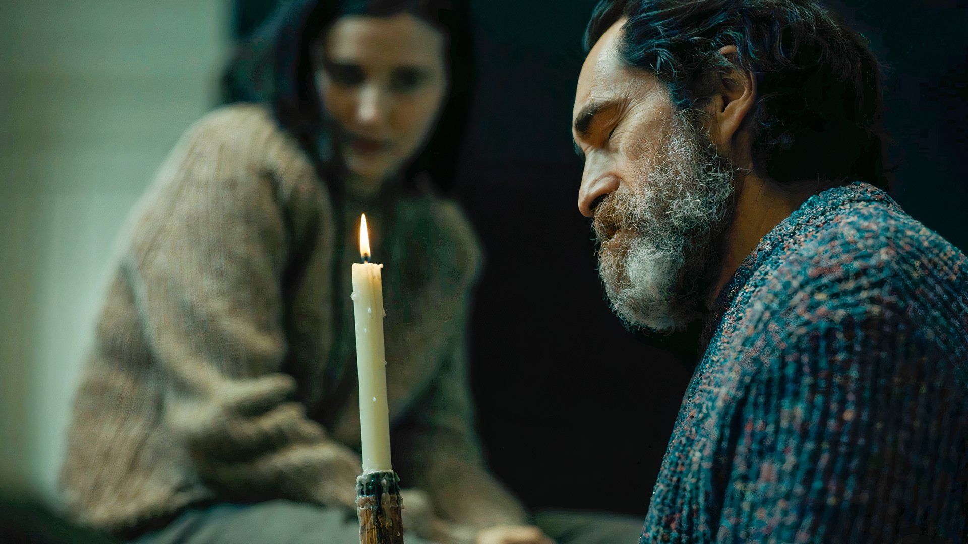 Demián Bichir as Ismael, sitting in a dark cabin in front of a candle beside Julia Goldani Telles as Emily, in Beacon