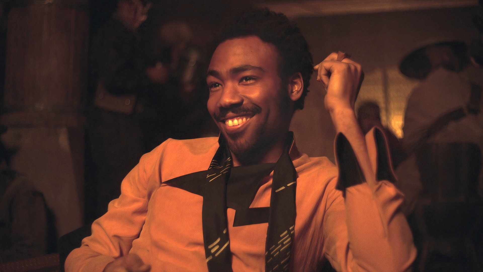 Donald Glover as Lando Calrissian in Solo: A Star Wars Story smiles as he sits at a table.