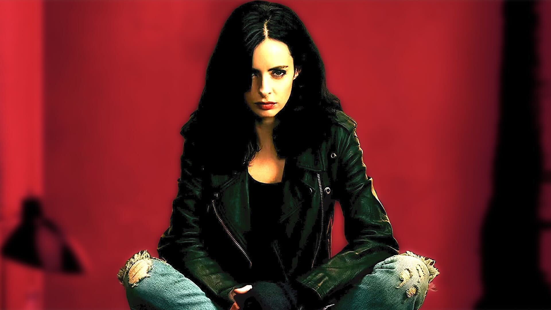 Krysten Ritter as Jessica Jones sitting with red background